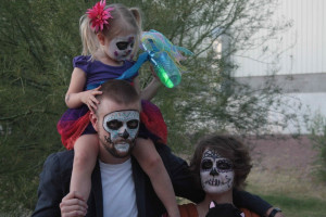 Family with dad and daughter on his shoulders, and mom with Day of the Dead skeleton face makeup
