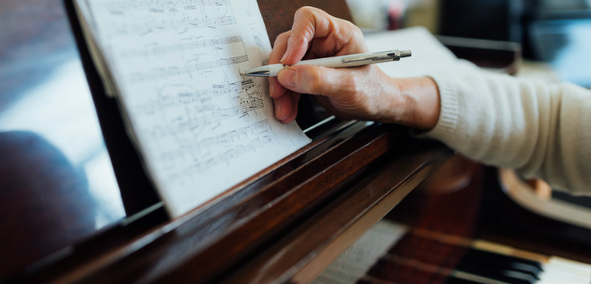 Student at piano taking notes on sheet music