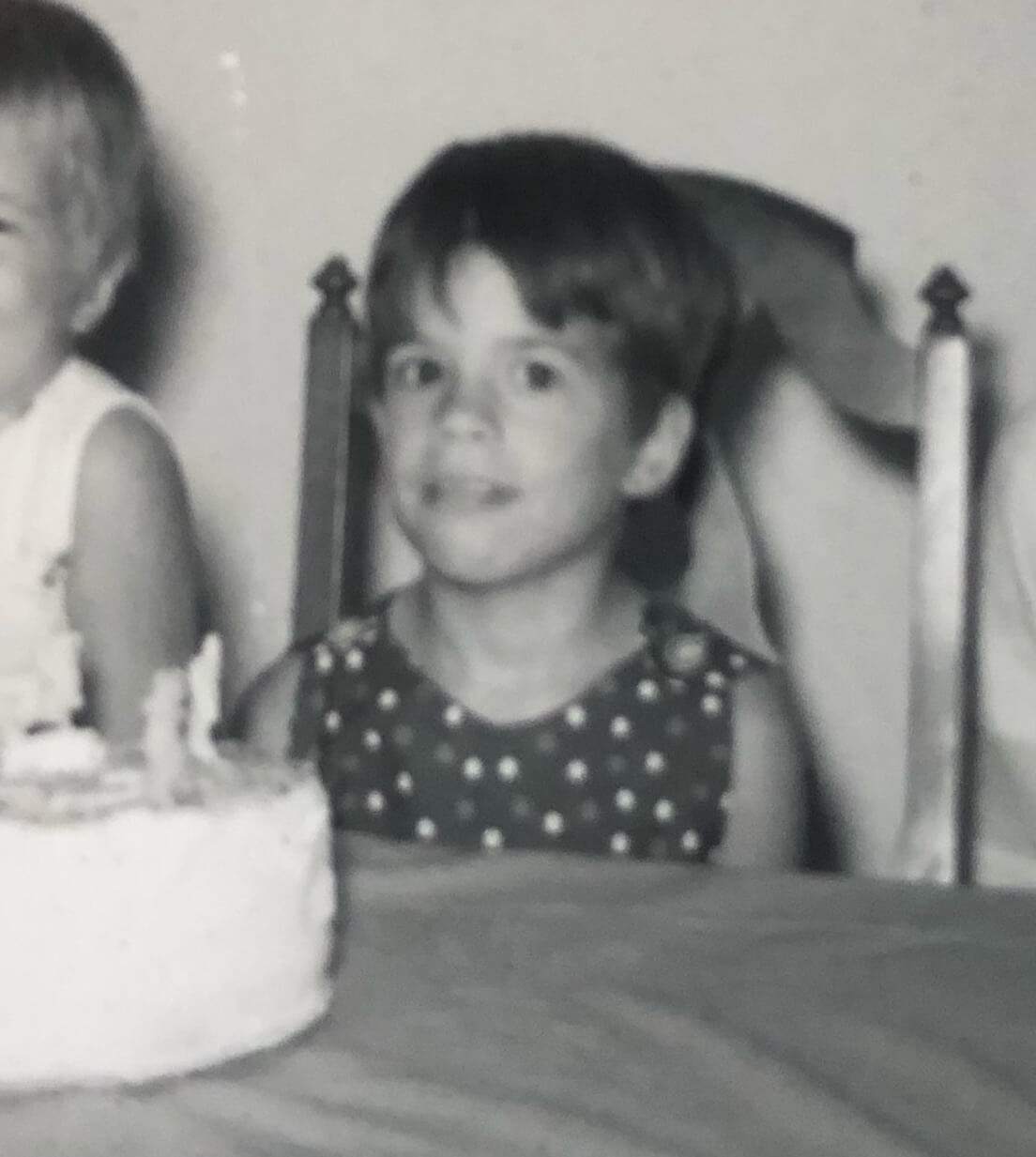 Nancy M. Williams at her sixth birthday sitting at a table with a birthday cake in white frosting.