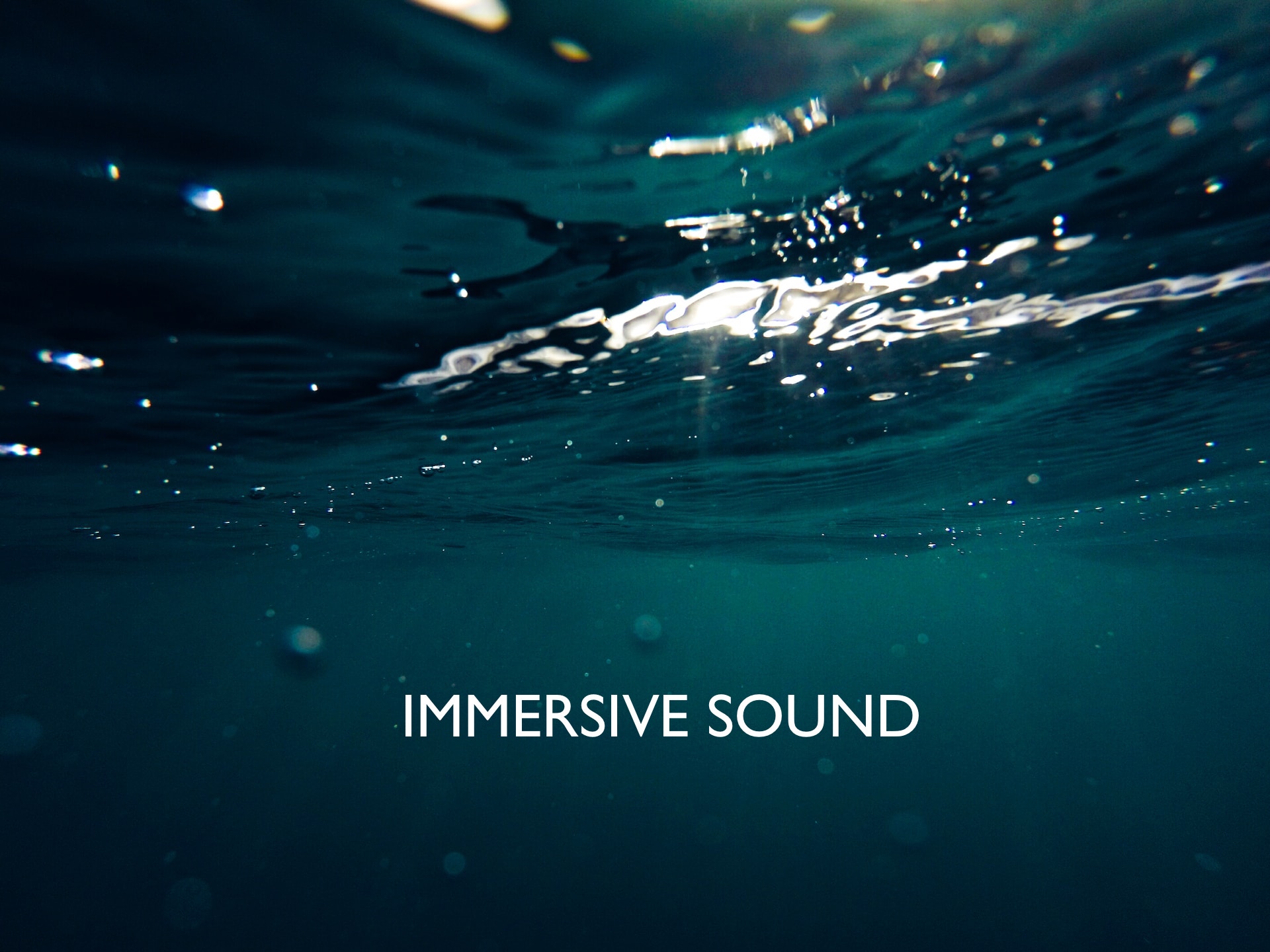 View of a lake underwater, with sunlight glinting on top, with the caption, "Immersive Sound"