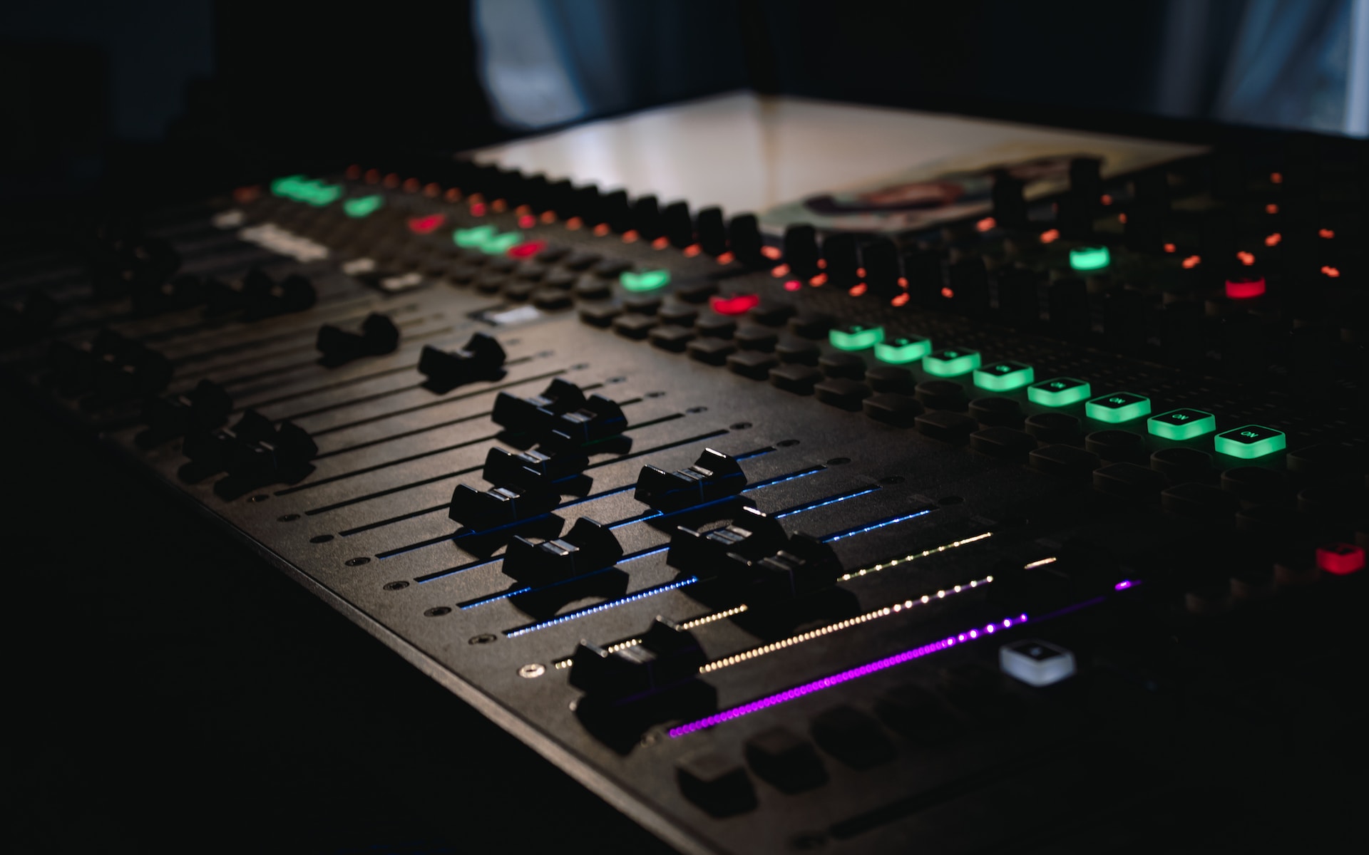An audio engineer's mixing board, with purple, green, and red glowing lights